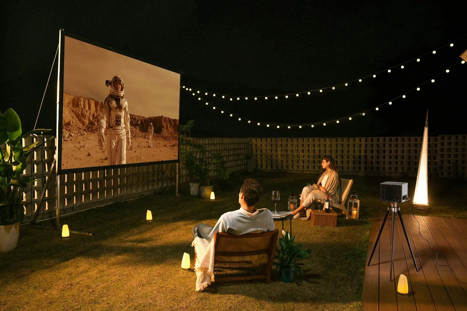 Couple watching a movie on an outdoor screen under string lights